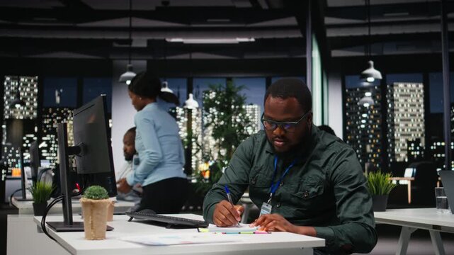 Male consultant engaged in handwriting notes for monthly reports, extracting essential highlights from finance documents and making a summary for business goals and upcoming tasks. Camera A.