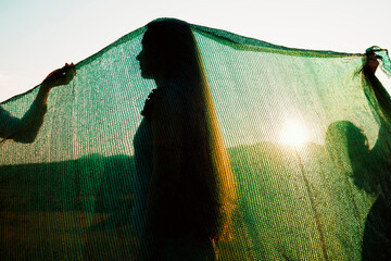 Silhouette of a Woman Behind Green Netting at Sunset in Nature