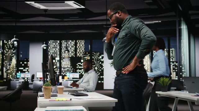 Black general manager thinking about a complex problem in a dark office late at night, concentrating on options at workstation. Reflecting logical solution through careful deduction. Camera A.