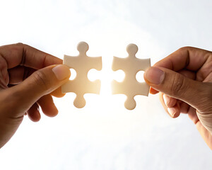 Hands holding two white puzzle pieces against a bright white background ready to be connected together