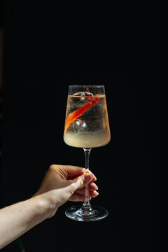 Sparkling cocktail with orange peel held against black background