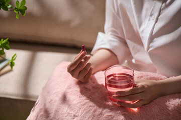 A person preparing to take a medication capsule with a glass of water