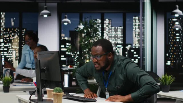 African american advisor focusing on a complex problem in a dark office at night, strategizing and envisioning options on desktop. Seeking a logical solution through careful deduction. Camera B.