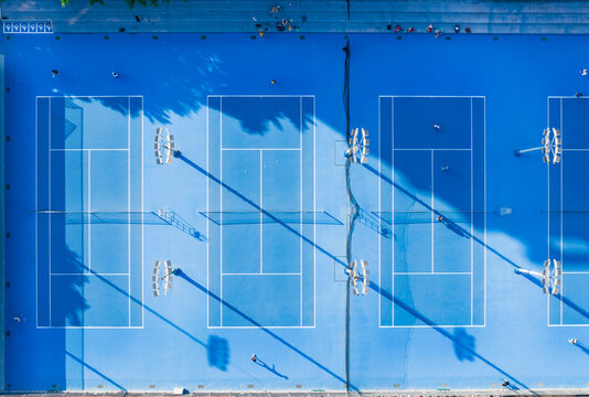 Aerial View of Blue Tennis Courts with Players and Shadows