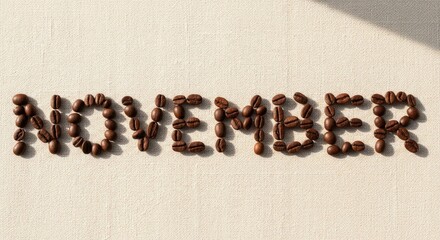 Brown coffee beans arranged to spell NOVEMBER on a cream-colored textured fabric surface with distinct shadows