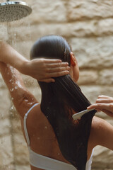 Woman washing long wet hair under a shower with comb in hand, natural skin tone, soft lighting, home bathroom setting, relaxing personal care moment.