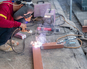 Sparks and smoke are visible as the worker uses a welding machine to fuse steel components.