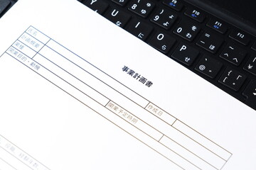 事業計画書 - 新規事業の立ち上げに先立ち、事業計画書を作成する起業家のイメージ
