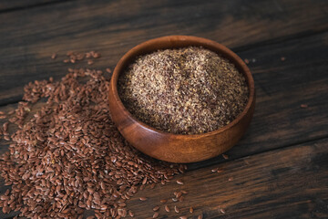 A rustic wooden bowl filled with nutritious ground flaxseed and whole seeds rests on a lovely wooden surface.
