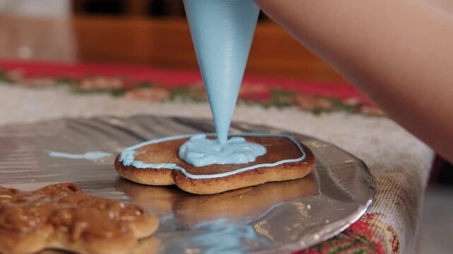 A close-up of a child hands decorating a mitten shaped gingerbread cookie with icing. A holiday baking workshop for children. Preparing for New Year's and Christmas.