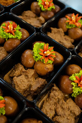 Indonesian beef rendang served with braised eggs in black plastic meal prep containers, decorated with lettuce and chili garnish, traditional spicy food for catering and delivery