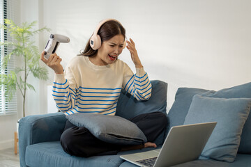 A young woman wearing headphones is playing a video game on her laptop, holding a controller with emotional expressions of joy, excitement, and frustration during gameplay.