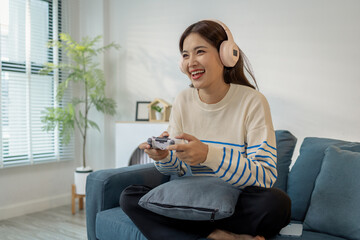 A young woman wearing headphones is sitting on a sofa while holding a game controller, showing joy, excitement, and focus as she plays a video game indoors.