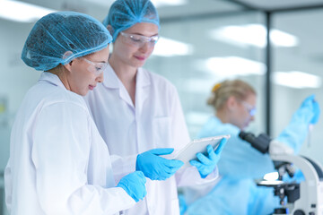 A senior scientist mentors a junior researcher, pointing at results on a digital tablet as they...