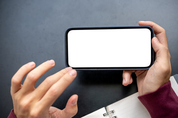 A man's hand holding white screen smartphone in horizontal with fingers hovering on table in a cafe.