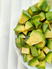 Green Avocado Pieces in a Ceramic Dish on a Textured White Surface