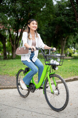 Obraz premium Full body shot of asian woman smiling while riding green bicycle strolling around in the nature park