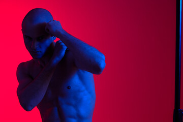 A dynamic man with a determined expression is posing against a vibrant red and blue background....