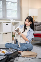 Asian woman plying with a cat while organize or packing luggage on a bedroom or living room's floor.