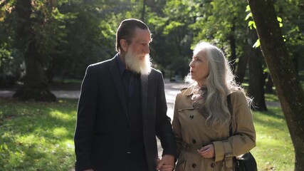 A beautiful senior couple walks hand in hand together in a beautifully sunlit park