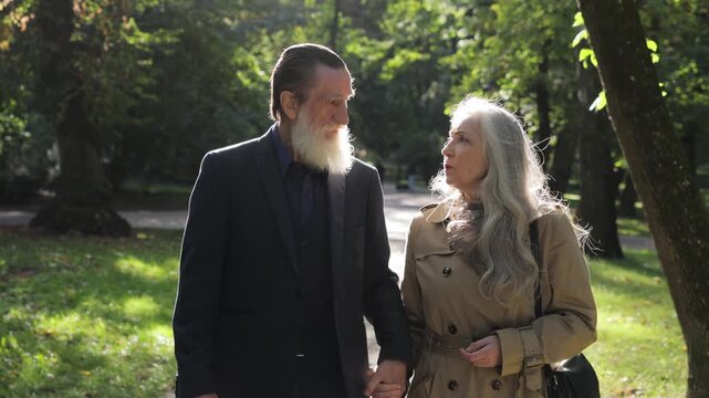 A beautiful senior couple walks hand in hand together in a beautifully sunlit park