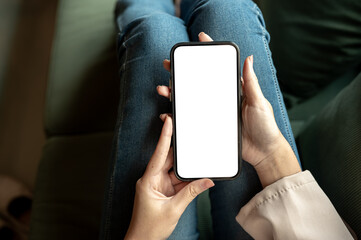Close up woman hands holding a blank screen smartphone while sitting on green sofa in cafe or lounge