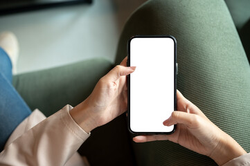 Close up woman hands holding blank screen smartphone while sitting on green sofa in a cafe or lounge