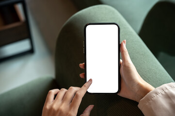Close up of woman hand pointing on blank screen smartphone sitting on green sofa in cafe or lounge