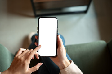 Close up of woman hand holding blank screen smartphone while sitting on green sofa in cafe or lounge