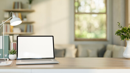 Fototapeta premium Blank screen laptop with file folder and cactus aside lamp on wooden table in living room or office.