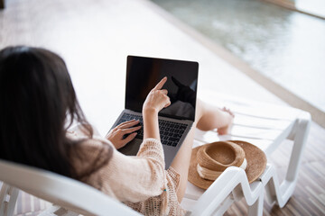 Young Hispanic Gen Z Woman in Swimwear Working on Laptop by Resort Pool During Summer Vacation.