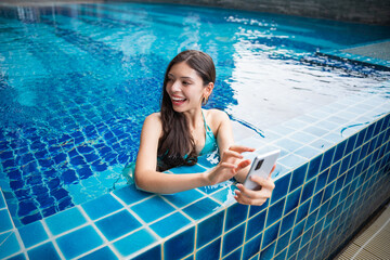 Young Hispanic Gen Z Woman Using Smartphone to Update Social Media by Resort Pool During Summer Vacation.