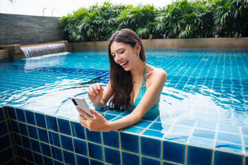 Young Hispanic Gen Z Woman Using Smartphone to Update Social Media by Resort Pool During Summer Vacation.