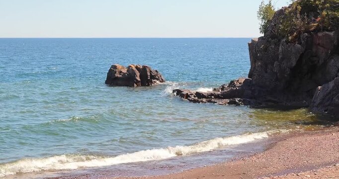 A beach, waves and trees at the rocky North Shore of Lake Superior in northern Minnesota on a sunny day.