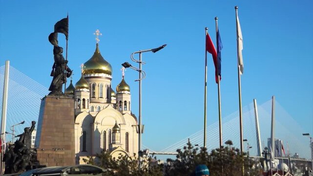 Central Square in Vladivostok, Russia, with the Orthodox cathedral, monument to Fighters for Soviet Power, flags, Zolotoy Bridge cables, clear day.
