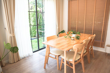 Modern dining room with natural wooden table, indoor plants, and sunlight through large glass...