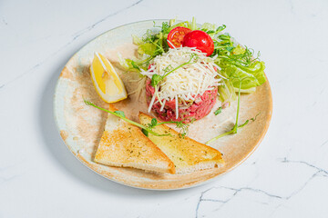 Fresh beef tartare with vegetables and toast garnished on a rustic plate indoors