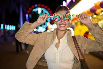 Woman smiling holding lollipops covering eyes at night fair