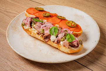 A mouthwatering sandwich with layers of meats, fresh greens, and spicy jalapeños sits on a plate