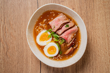 A savory bowl of rich broth, tender beef, and soft-boiled eggs on a wooden table