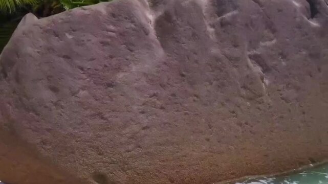 Close-up of rough brown seawall encrusted with barnacles at the foamy waterline, small wave splash in foreground and slice of blue sky in background, concept of marine erosion and coastal maintenance