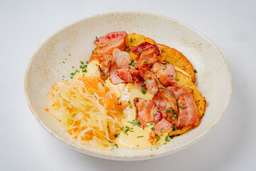 A warm bowl filled with golden pancakes topped with crispy bacon and served alongside sauerkraut
