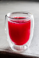 Vivid red beverage fills a glass, capturing light with refreshing allure on a wooden surface