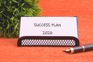 A note reading Success Plan 2026 sits in a holder, with a pen to its side and decorative greenery....