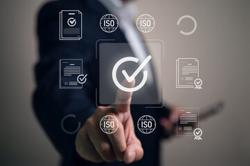 Businessman pointing at a checkmark icon for quality assurance and ISO certification. The virtual interface represents compliance with international standards, audits, and quality management.