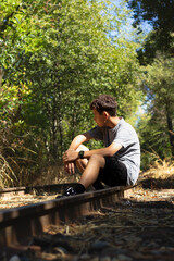 Boy Sitting by Railway Tracks Surrounded by Greenery, Enjoying Nature on a Sunny Day