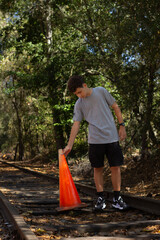 Teenager Interacts With Traffic Cone Along Abandoned Railway Track in Forest During Sunny Afternoon