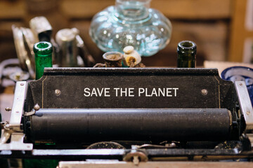 A vintage typewriter displays the phrase SAVE THE PLANET. Antique bottles and various containers decorate the area, suggesting a focus on recycling and historical awareness