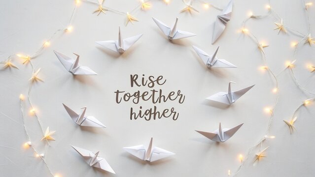 White paper cranes arranged in a circle with fairy lights and inspirational quote about unity and progress on plain background