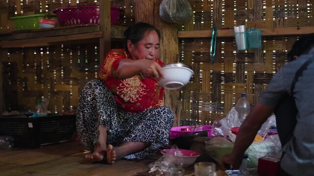Southeast Asian woman carefully preparing a home-cooked meal inside a traditional rural kitchen with rustic bamboo walls